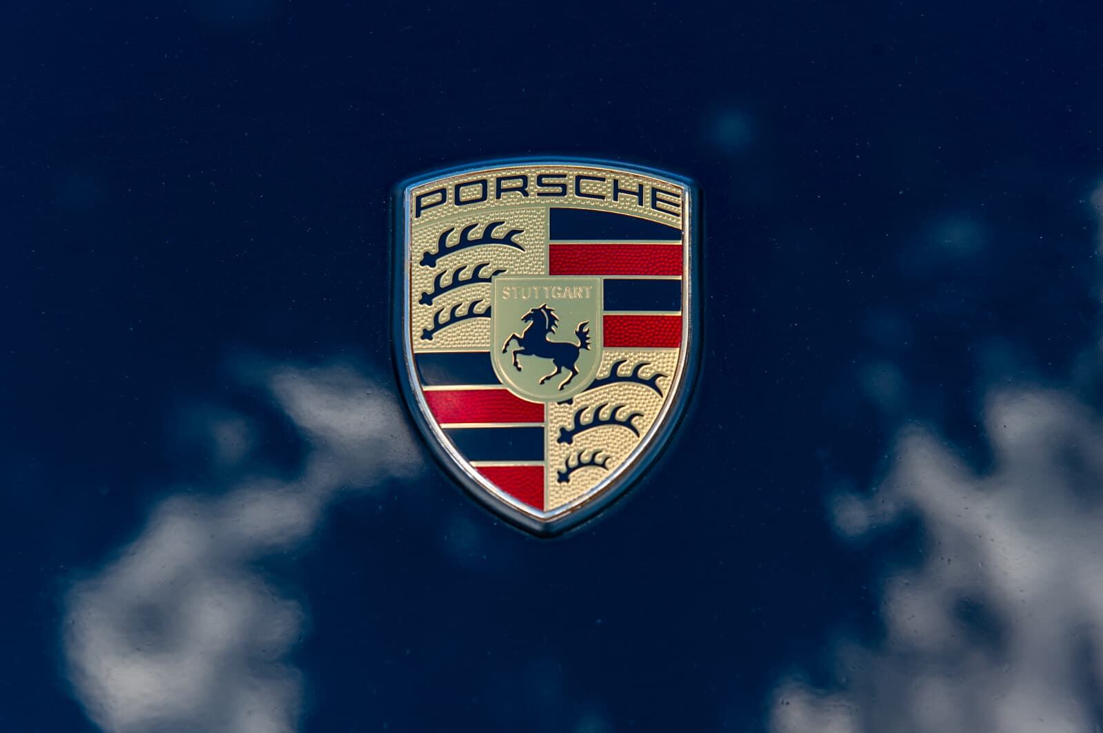 Stemma Porsche sul cofano anteriore, con il cielo riflesso nella vernice Stemma Porsche sul cofano anteriore, con il cielo riflesso nella vernice